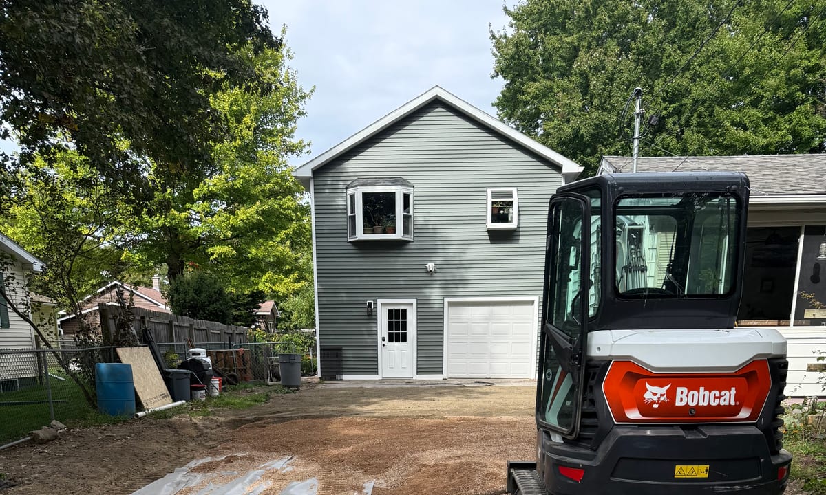 Magee's Excavation mini excavator parked on a gravel driveway beside a Vermont home
