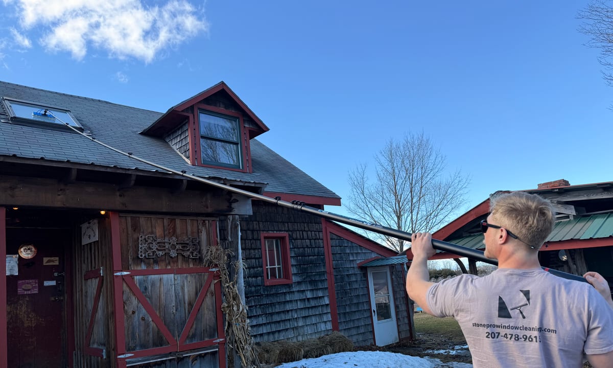 Gage Stone washing an exterior window on a rustic Vermont building with a water-fed pole